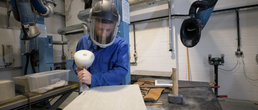 A person carving into a piece of stone in a workshop