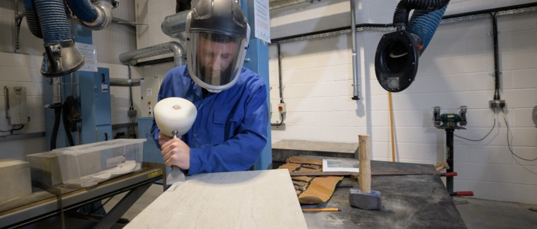 A person carving into a piece of stone in a workshop