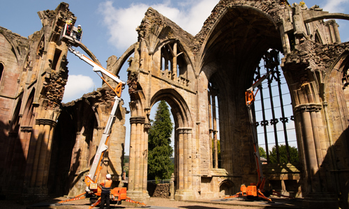 Engineers wearing personal protective equipment (PPE) while inspecting the masonry of an abbey from the top of two cherry pickers