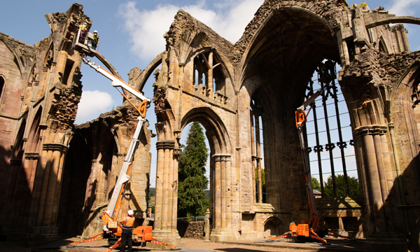 Engineers wearing personal protective equipment (PPE) while inspecting the masonry of an abbey from the top of two cherry pickers