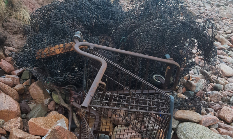 A shopping trolley lying on its side on a beach, entangled with fishing net