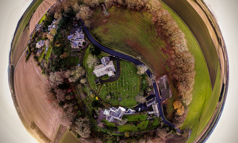 A circular bird's eye view of a small farmhouse sitting amongst fields 
