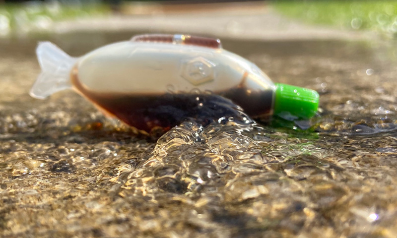 A plastic soy sauce container shaped like a fish in lying in a puddle of water