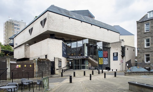 The exterior of Dundee Rep Theatre. Entry is made through a revolving door underneath a glass façade
