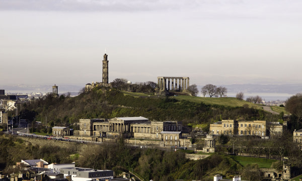 Landscape photo of monuments on a hill and houses. View of Calton Hill. 