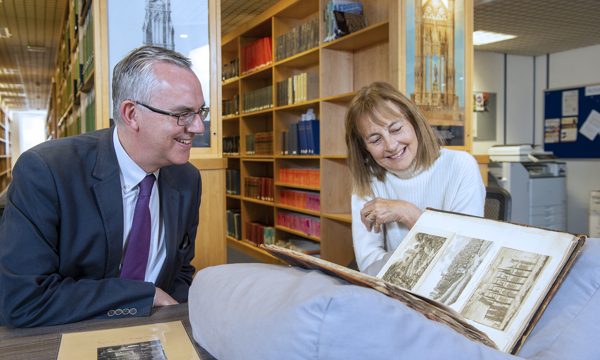 a man and woman sitting in a library pore over a large book with illustrations or Rosslyn Chapel