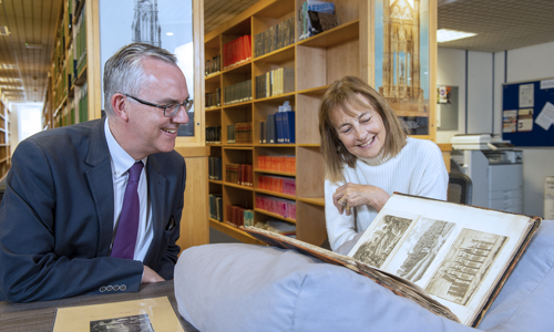 a man and woman sitting in a library pore over a large book with illustrations or Rosslyn Chapel