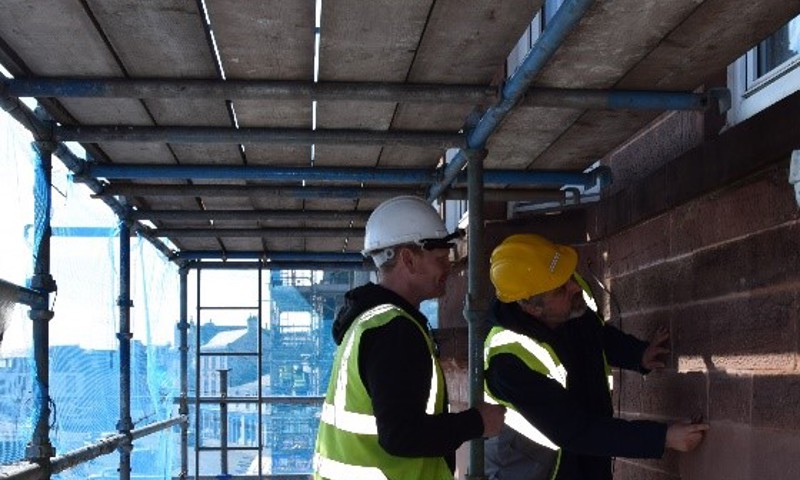 Workmen on scaffolding repairing a wall