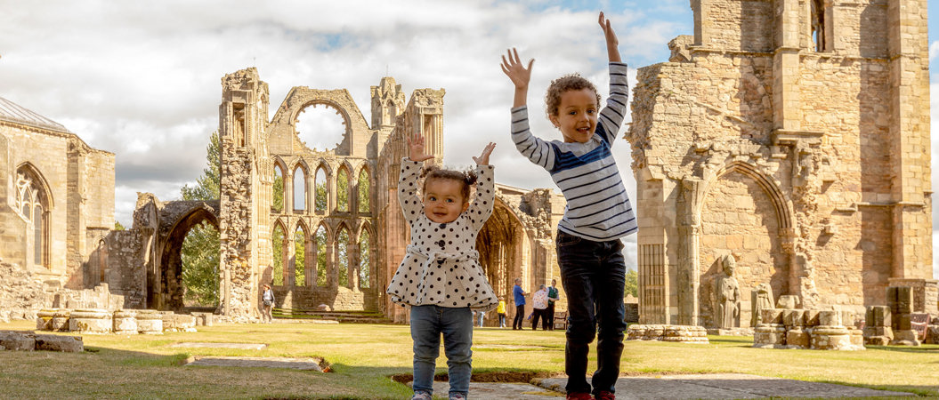 Two children in the grounds of Elgin Cathedral with their arms in the air