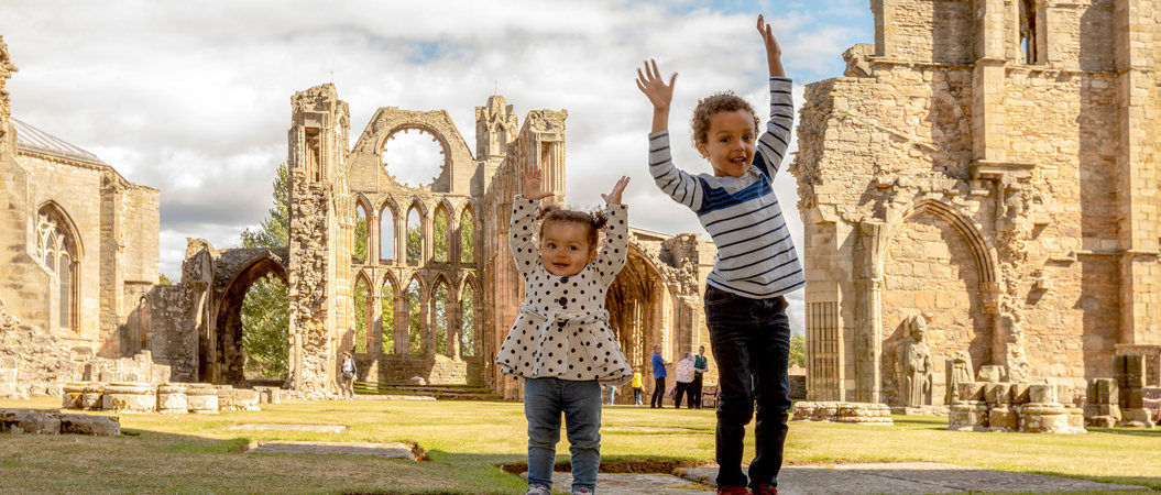 Two children in the grounds of Elgin Cathedral with their arms in the air