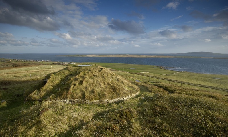 A grass-covered chambered cairn in a coastal location 