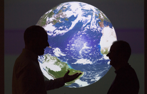 Two people talk silhouetted against a large image of earth