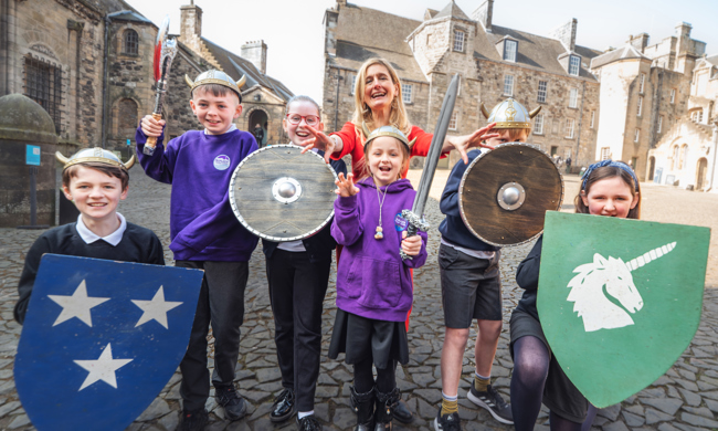 Cressida Cowell and children with medieval shields stand in the courtyard at Stirling Castle 