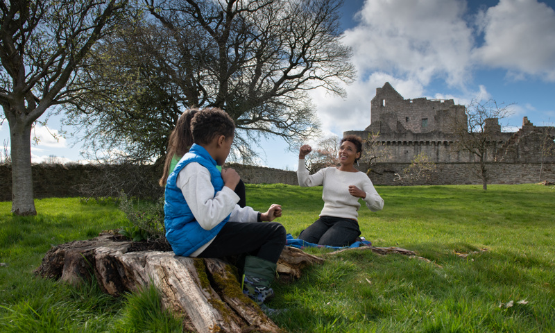 Mara Menzies tells a story to two children outside a castle.