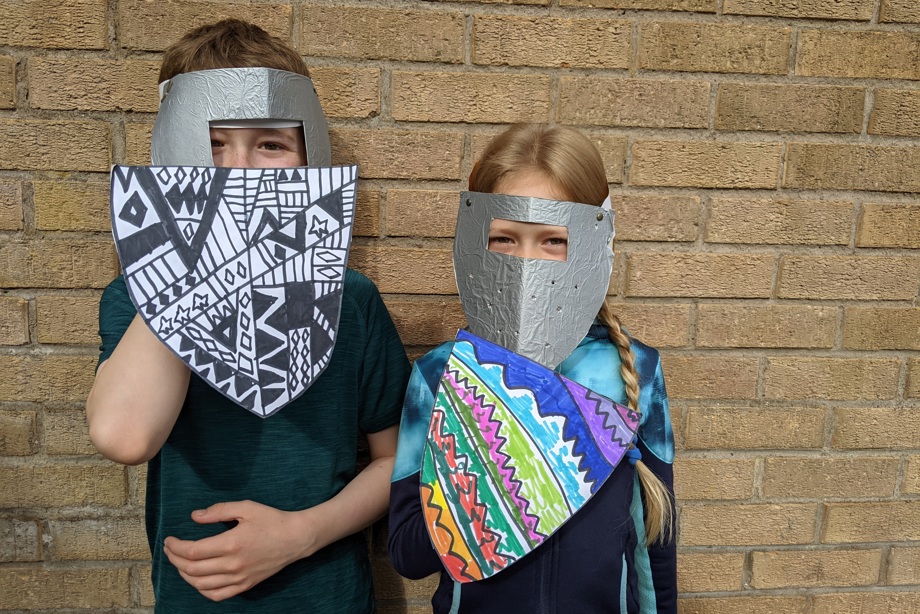 Two children holding home-made shields and wearing home-made paper helmets