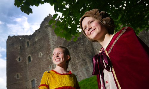 Two young girls in renaissance costume stand in front of Doune Castle
