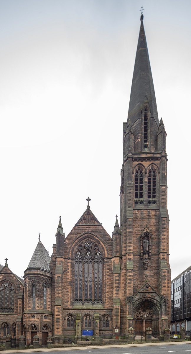 The exterior of a large gothic church with a tall spire on a slightly sloping city street