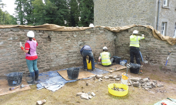 People wearing high visibility jackets and hard hars working on a brtick wall
