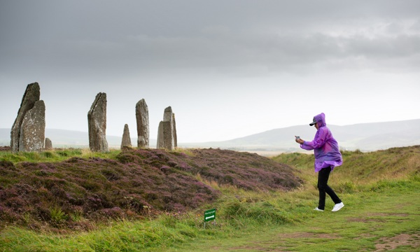 A visitor holding a smart phone approaches a large stone circle