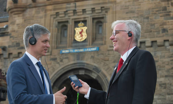 Two people standing in front of Edinburgh Castle listening to an audio guide