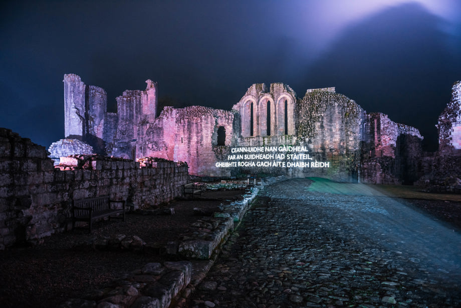 Gaelic poetry is projected onto a castle at night. 