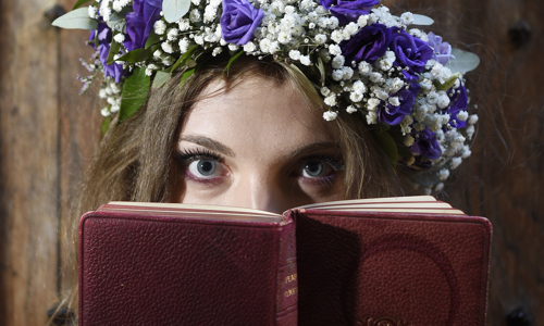 Midsummer fairy actor with flower headdress looks over a leather bound book. 