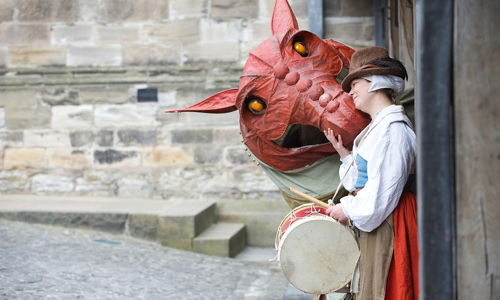 Photo of a person in re-enactment clothing and a model dragon.