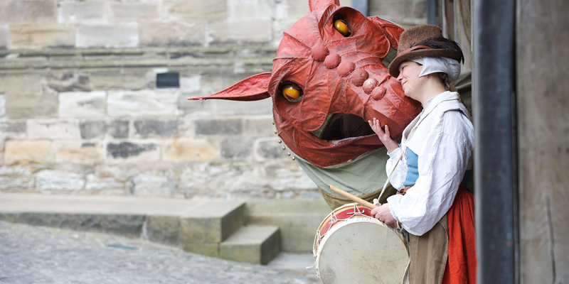 Photo of a person in re-enactment clothing and a model dragon.