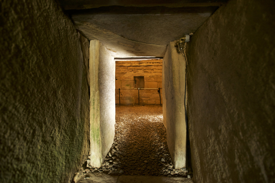 Light passing through a long, narrow stone corridor into a stone chamber