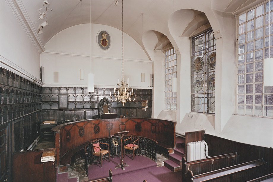Inside a chapel with carved wooden pews and wall panelling, and stained glass windows