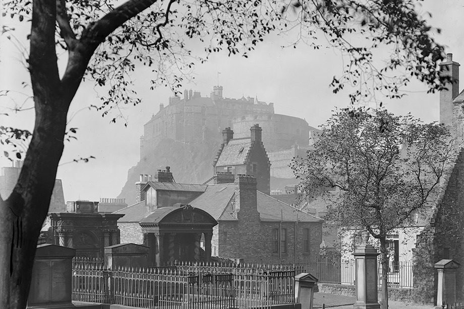 Shrines and grayestones in a churchyard, with Edinburgh Castle in the background on a hill