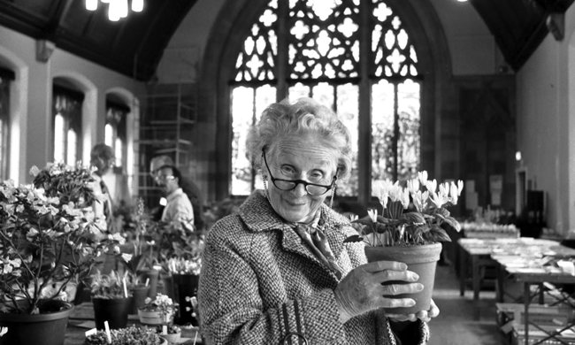 An older woman holding up a pot of flowers inside a church