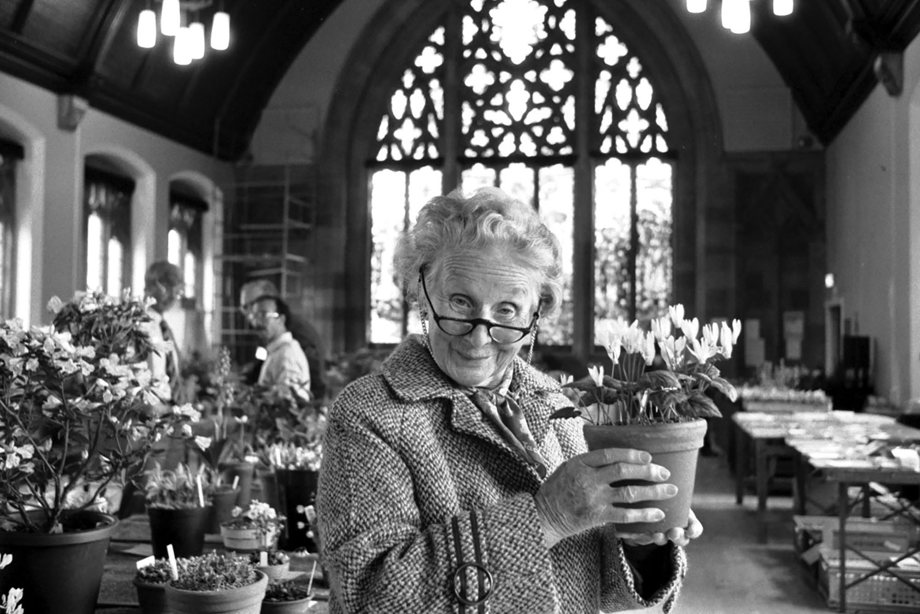 An older woman holding up a pot of flowers inside a church