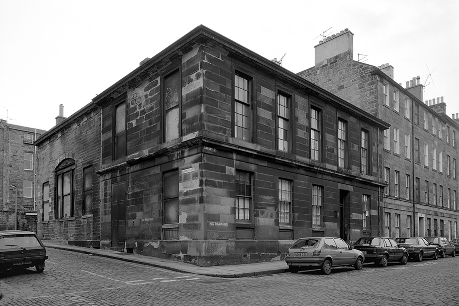 A large, square stone tenement building with cars parked outside on the street. Image reference number: SC_981951