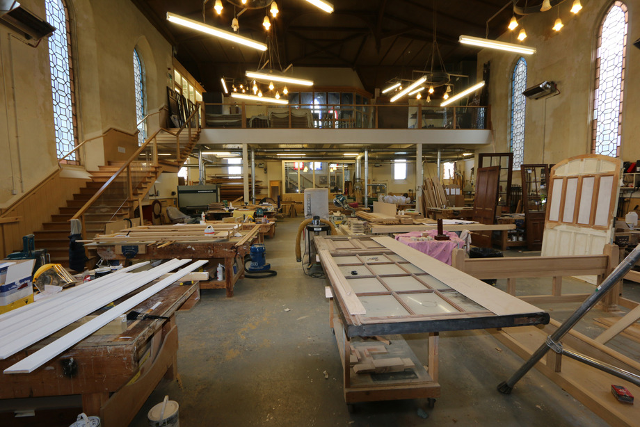 Woodworking tables and equipment inside a church with many large, ornate windows