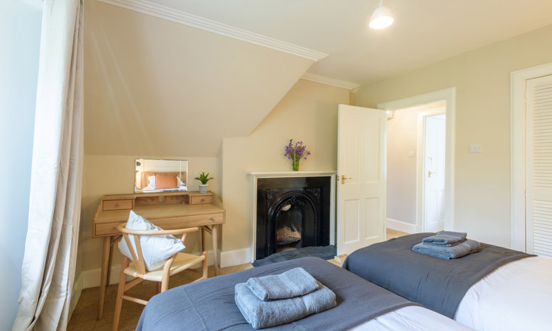Twin bedroom in Meadowbank Lodge, bright with pale yellow walls and an old fireplace