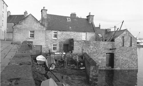 Picturesquely grouped house and stores built on a harbour front in SHetland.