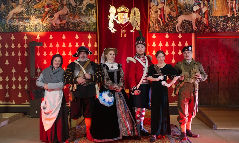 Costumed reenactors from various historical eras pose for a group photo in the Great Hall of Stirling Castle