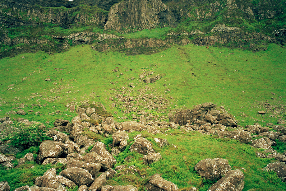 A landscape including a round plaform of stones in the foreground with cliffs containing a cave in the background. 