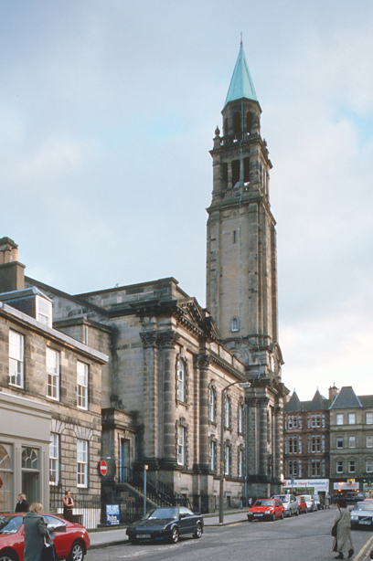 A stone church with a tall spire, surrounding by city tenement buildings, on a busy street. Image reference number: 000-000-522-423-R