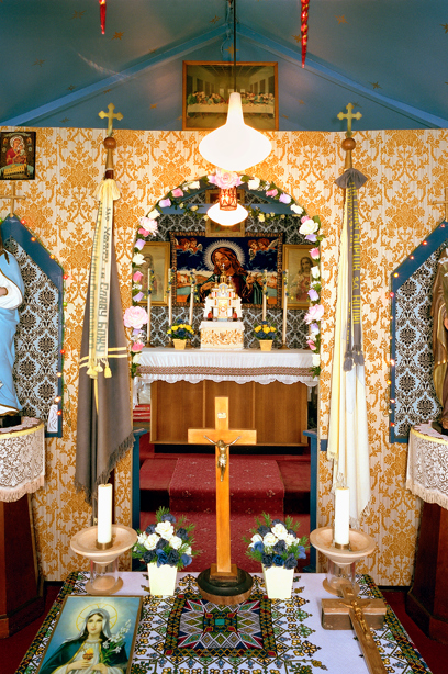 An altar with blue and yellow, busy patterned walls, filled with objects including flowers and crosses. Image reference number: SC_908232