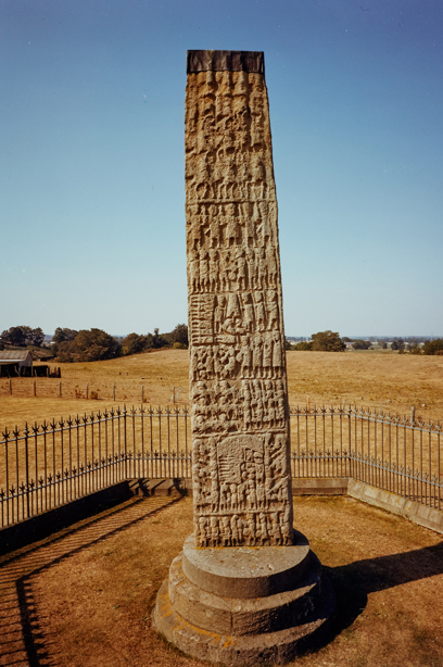 A standing stone in a field, covered in carvings of people