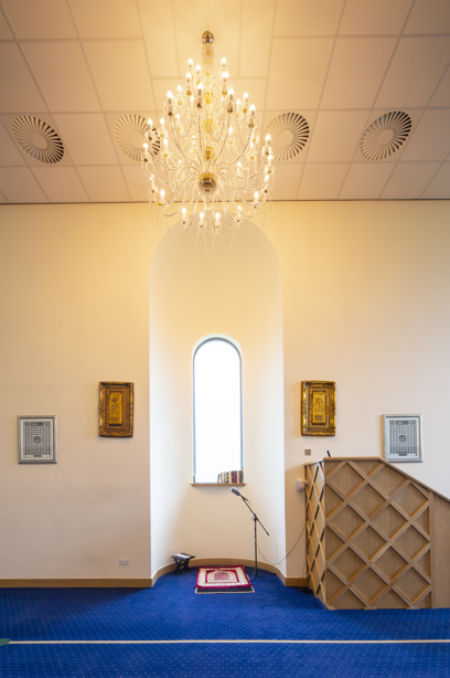 A prayer area, in front of a tall, curved dormer window, and a large chandelier hanging above the prayer mat. Image reference number: DP_359517