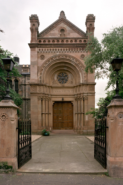 The entrance to a stone synagogue with two large wooden double doors, and lots of stonecarving detail on the building. Reference no: SC_441364