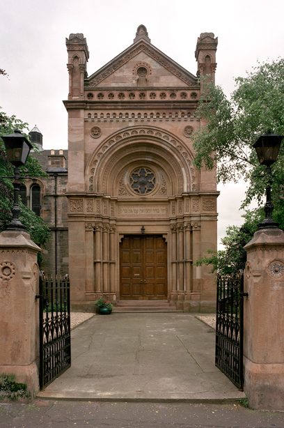 The entrance to a stone synagogue with two large wooden double doors, and lots of stonecarving detail on the building. Reference no: SC_441364