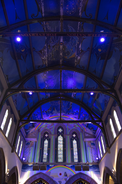 A church with tall stained glass windows, a curved ceiling and murals painted on the walls and ceiling