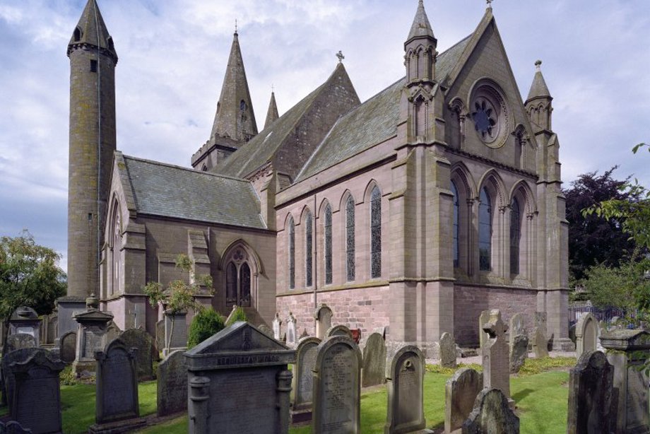A large stone cathedral with a small roundtower attached, and many gravestones in the grounds