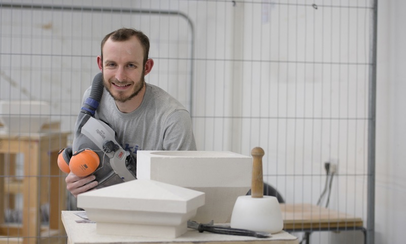 A stonemason posing with his equipment, tools and a finished piece of work