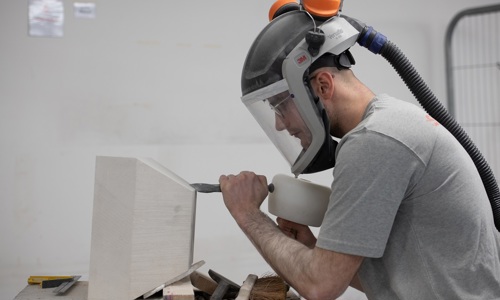 A stonemason wearing protective equipment works on a block of white stone