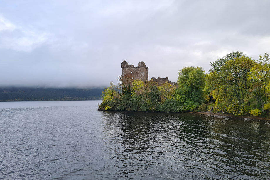 Urquhart castle is surrounded by trees and overlooks a calm looking Loch Ness